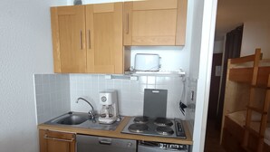 Een compacte keuken met houten kastjes, een geïntegreerde vaatwasser, een koffiezetapparaat en een fornuis.