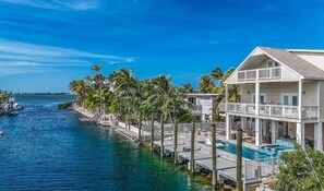 A waterfront property with a pool, docked boats, and palm trees. - Manatee Watch | 5 bedrooms, pool, ocean access (Big Pine Key)