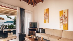 Un salon avec un canapé, une table basse et un téléviseur. De grandes fenêtres offrent une vue sur la mer.
