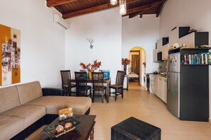 Ein modernes Wohnzimmer mit Sofa, Esstisch, Stühlen und einer Küchenzeile inklusive Kühlschrank und Bücherregalen.