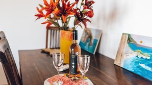 Une table à manger avec une bouteille d’alcool, deux verres et un vase de fleurs.