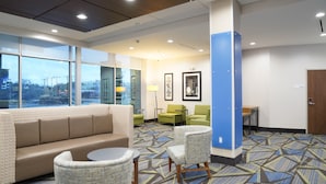 A hotel lobby with a sofa, chairs, a small table, a lamp, and framed artwork on the wall. - Holiday Inn Express & Suites Dallas Central Market Center by IHG (Dallas)