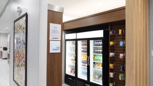 A modern interior with a refrigerator stocked with beverages and snacks, a wooden panel wall, and a framed artwork. - Holiday Inn Express & Suites Dallas Central Market Center by IHG (Dallas)