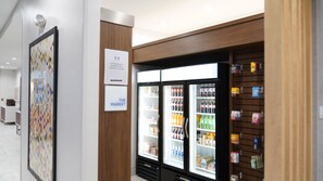 A modern interior with a refrigerator stocked with beverages and snacks, a wooden panel wall, and a framed artwork.