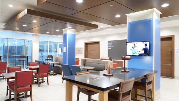 A modern indoor space with tables, chairs, a sofa, and a television mounted on the wall. - Holiday Inn Express & Suites Dallas Central Market Center by IHG (Dallas)