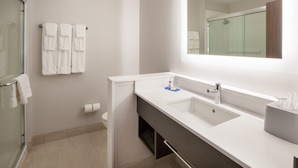 A modern bathroom with a glass shower enclosure, a white sink with a mirror above it, and a towel rack with multiple towels. - Holiday Inn Express & Suites Dallas Central Market Center by IHG (Dallas)