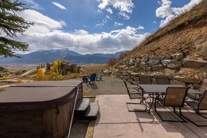 An outdoor patio with a hot tub, seating area, and a scenic view of mountains. - Luxurious Mt CB Home | 6 Bedroom | Best Views in CB | Hot Tub | Gas Grill (Mt. Crested Butte)