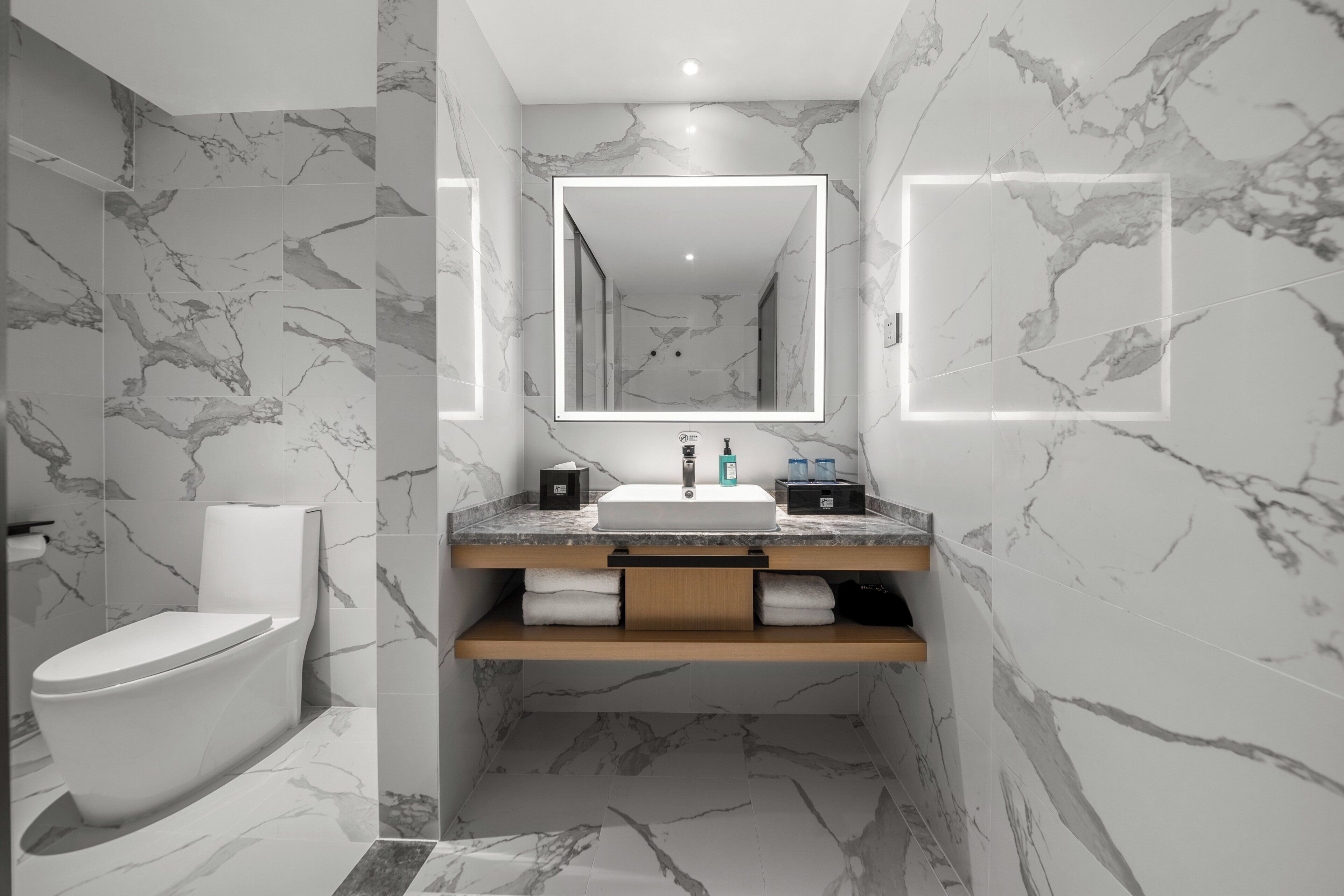 Une salle de bain moderne avec un sol en marbre, un lavabo blanc et un grand miroir.