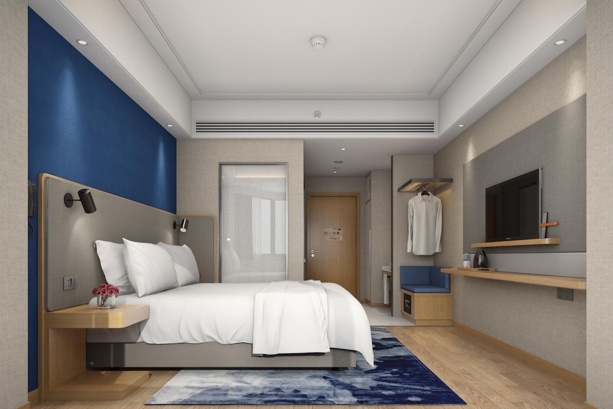 A modern bedroom with a bed, bedside tables, a TV, and a bathroom visible through an open door.