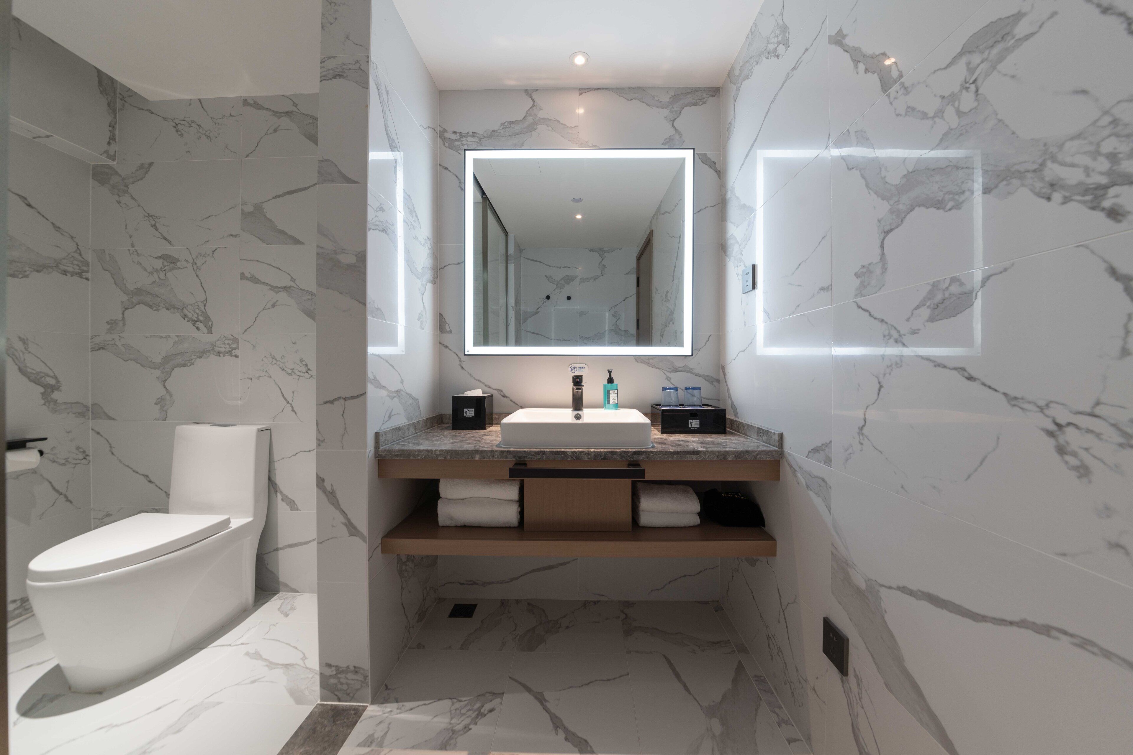 Un baño moderno con suelo de mármol, inodoro blanco, lavabo con espejo y un perchero para toallas.
