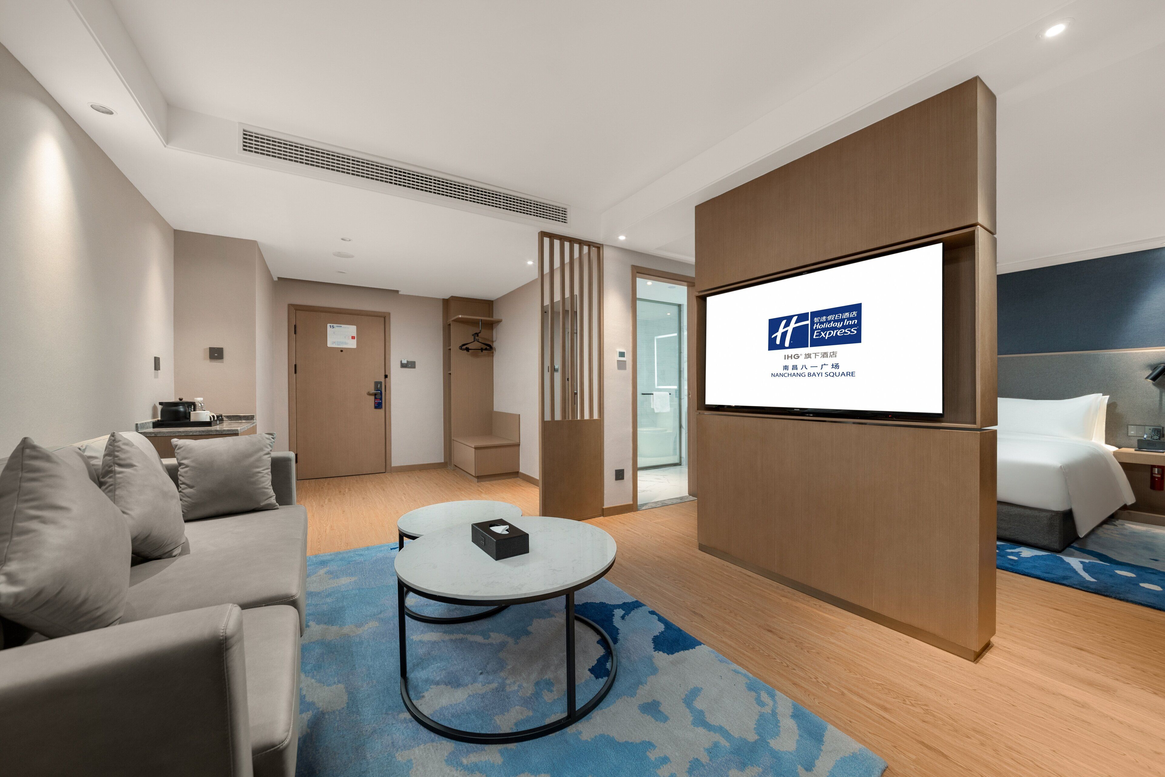 Una habitación de hotel moderna con una televisión de pantalla plana grande, un sofá, una mesita y una cama.