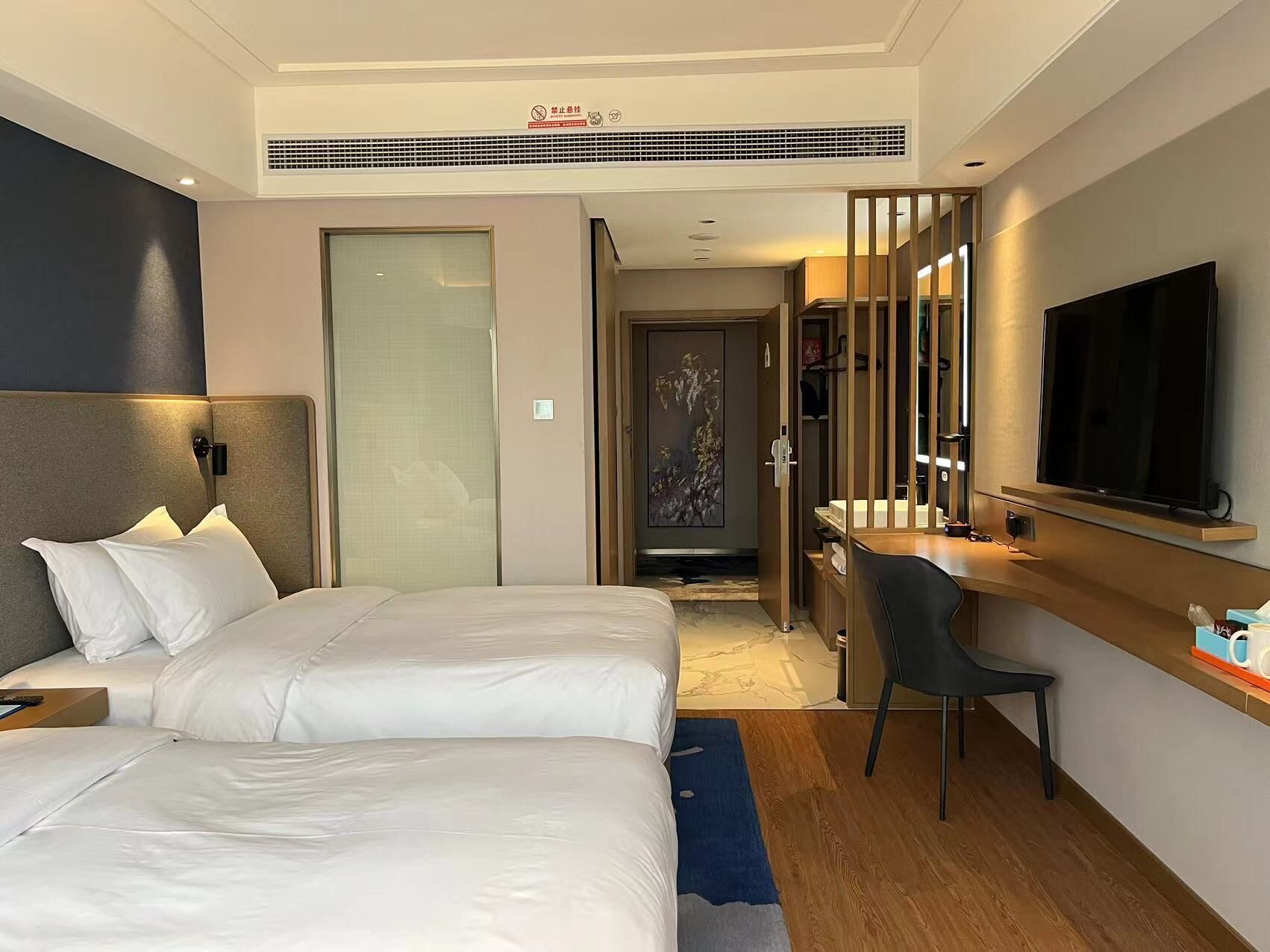 A hotel room with two beds, a desk, a chair, a TV, and a bathroom.