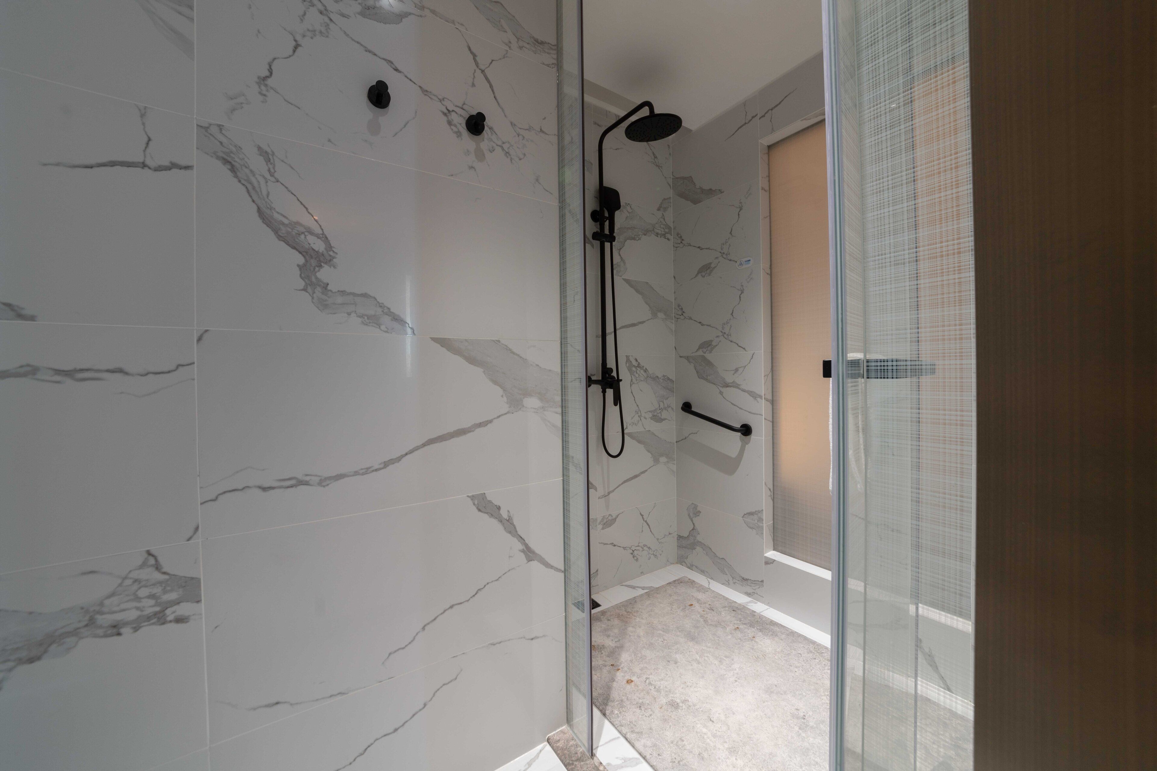 A modern bathroom with marble walls, a glass shower enclosure, and a wooden door.