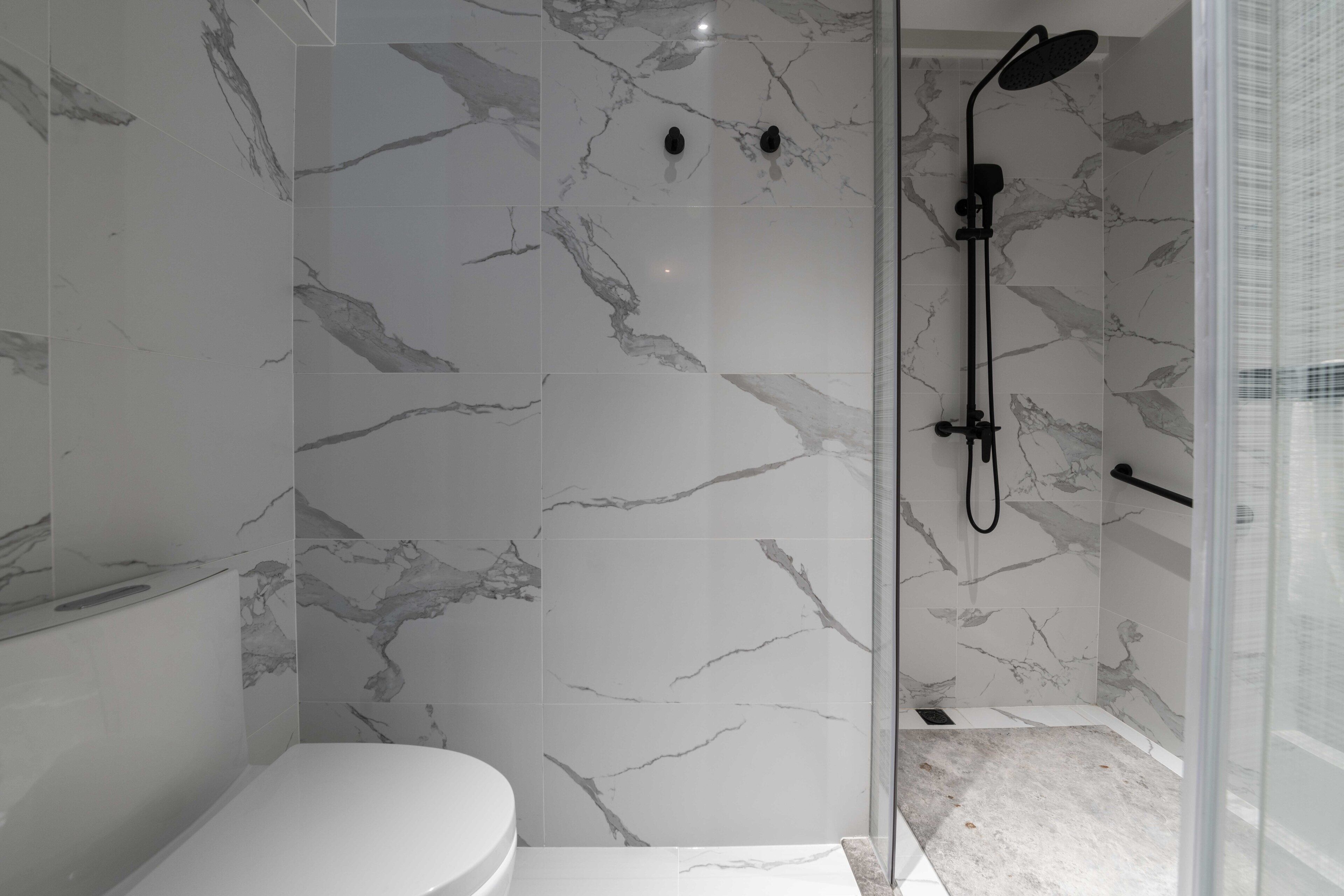 Un baño moderno con inodoro, ducha con cabezal de mano y paredes con diseño de mármol.