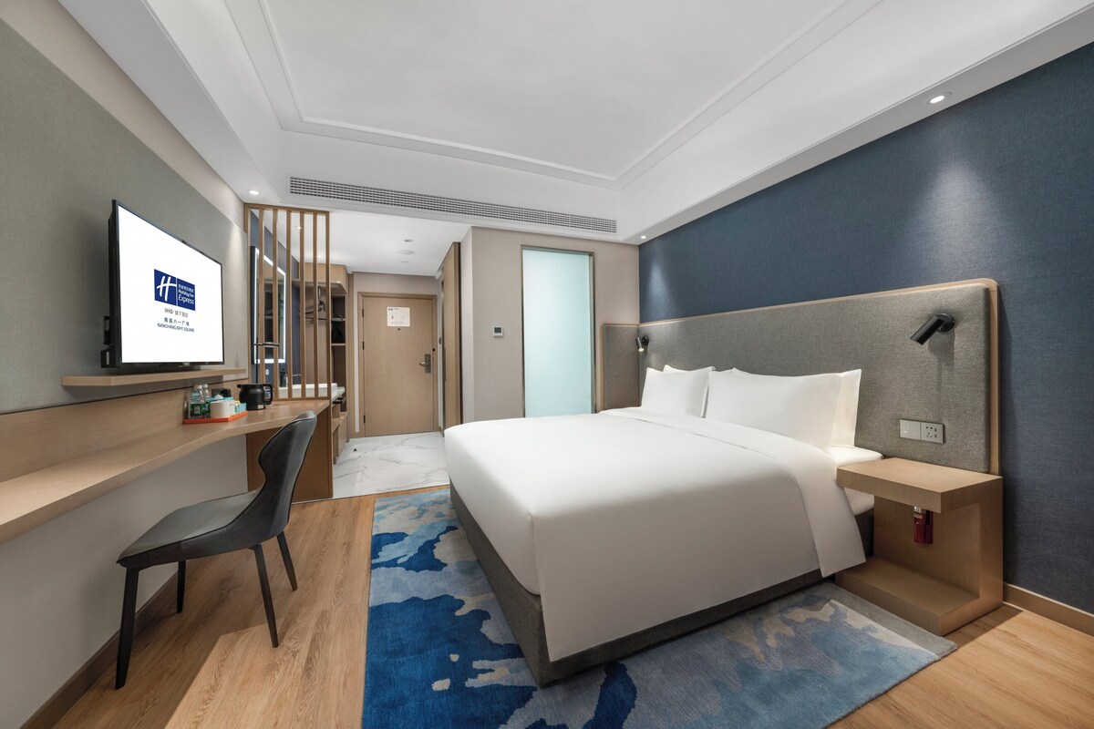A hotel room with a bed, a desk, a chair, a television, and a nightstand.