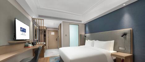 A hotel room with a bed, bedside tables, a desk with a chair, a television, and a wardrobe.