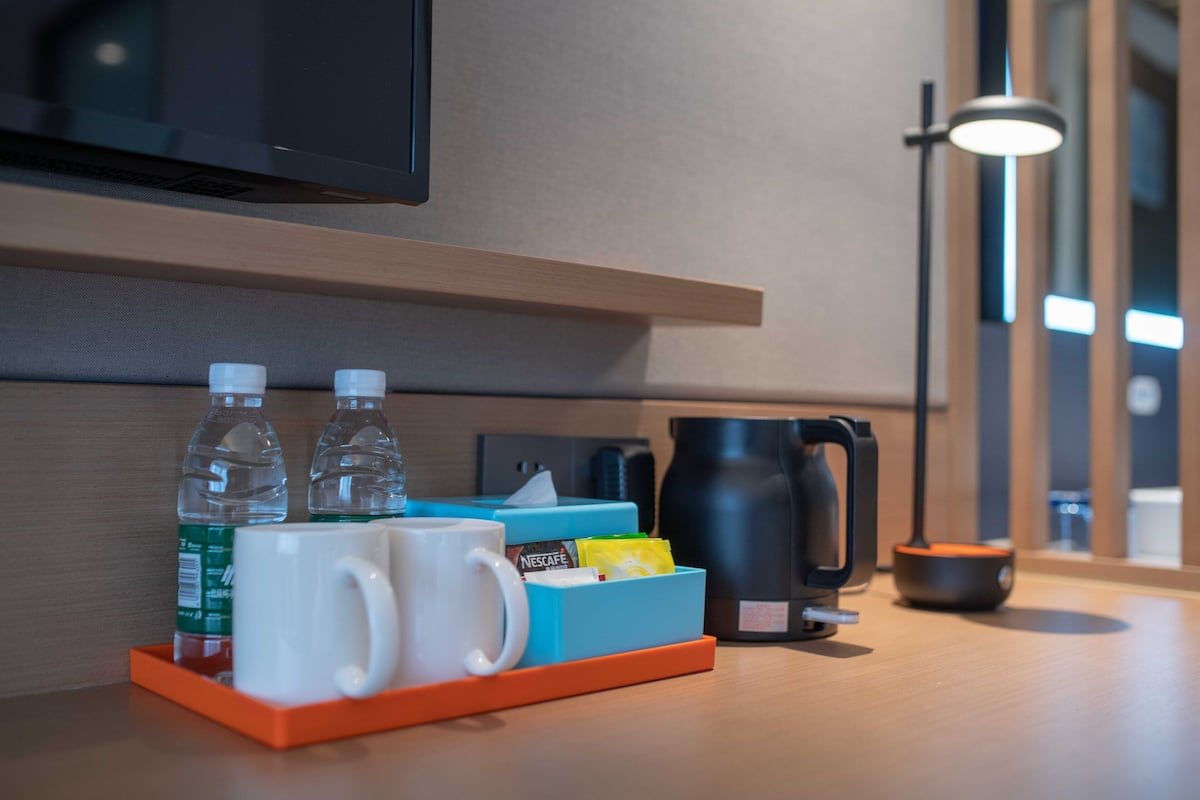 A hotel room with a coffee maker, two water bottles, a mug, and a tissue box on a wooden table.