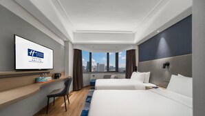 A modern hotel room with a large bed, a desk, a chair, and a TV displaying a hotel logo. - Holiday Inn Express Nanchang Bayi Square by IHG (Nanchang)