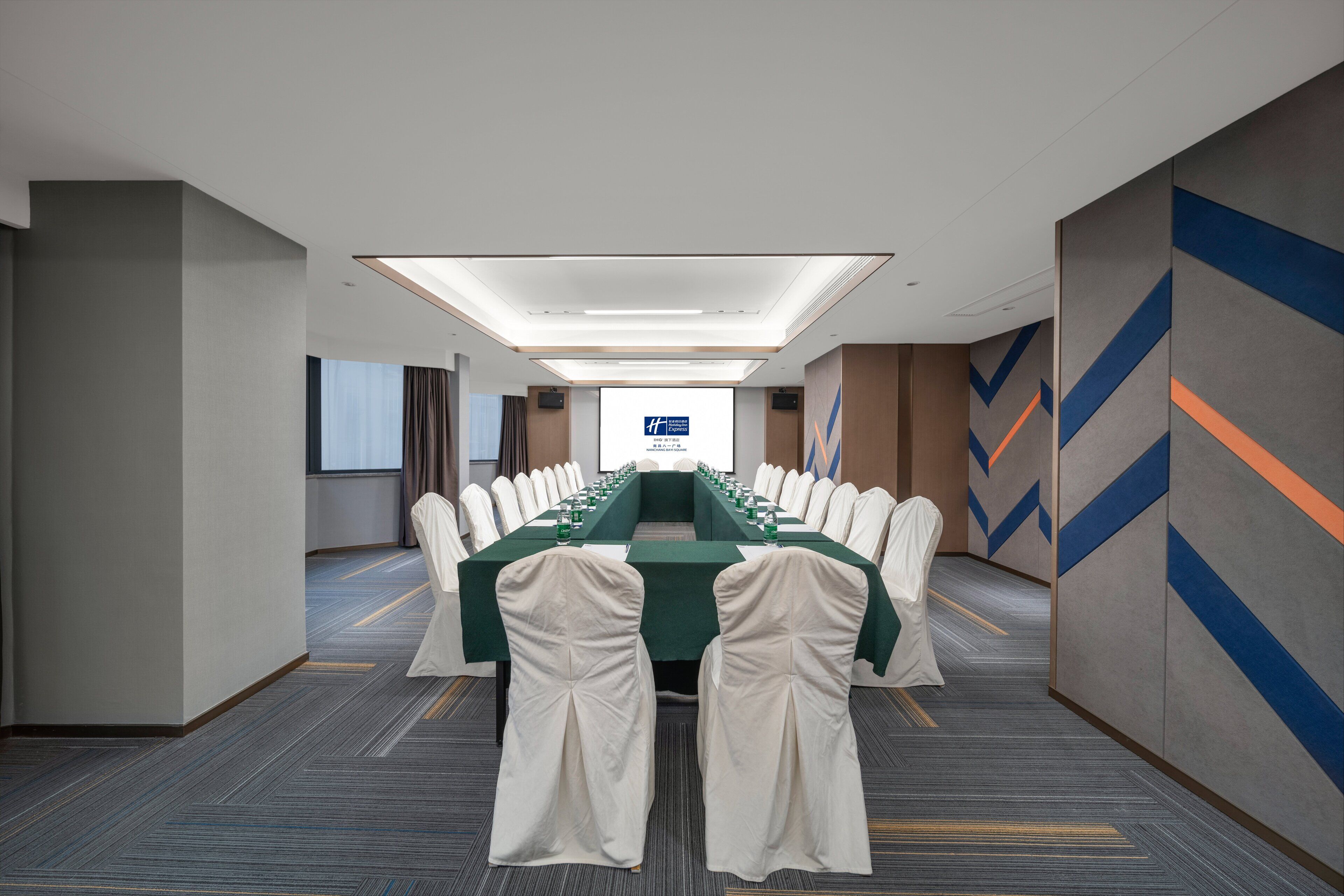 A conference room with a long table, white chairs, and a projector screen at the front.
