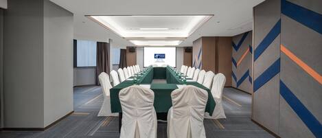 A conference room with a long table, white chairs, and a projector screen at the front.