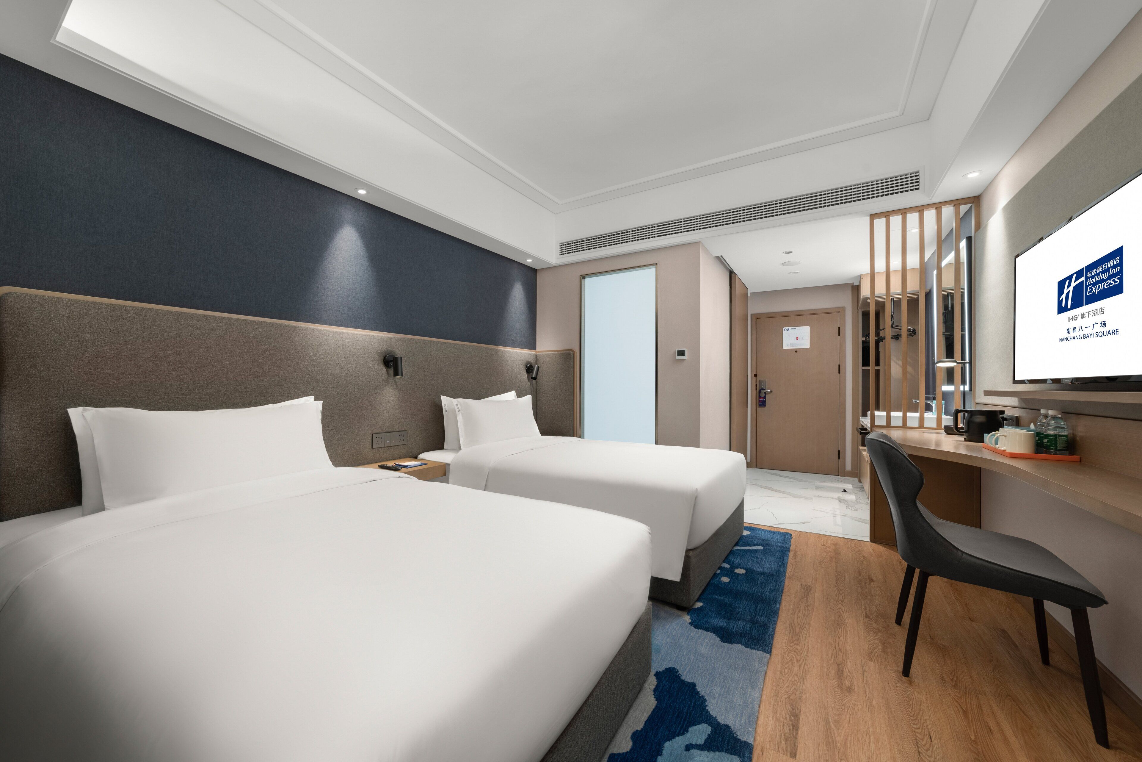Quarto de hotel com duas camas, uma escrivaninha, uma cadeira e uma televisão.