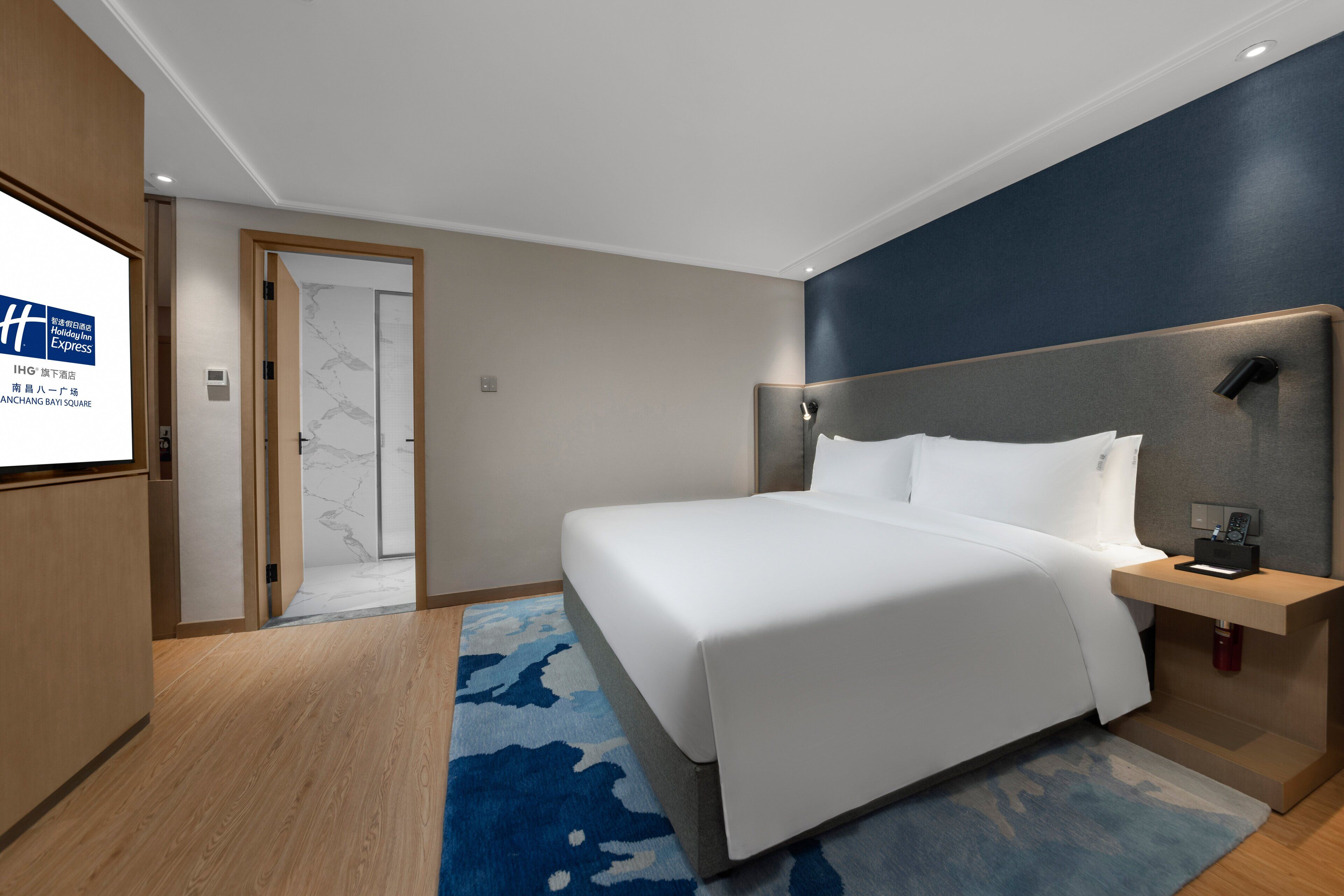 Une chambre d’hôtel moderne avec un grand lit, une table de chevet en bois et un tapis à motifs bleus.