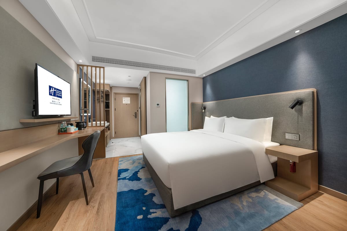 A hotel room with a bed, a desk, a chair, a television, and a nightstand.