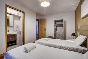 Two single beds with neatly folded towels, a wardrobe, and a nightstand with a lamp and mirror.