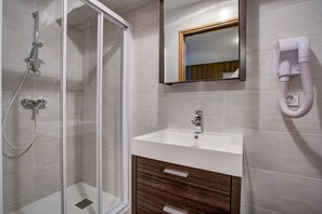 Bathroom features a glass-enclosed shower, handheld showerhead, and wall-mounted faucet.