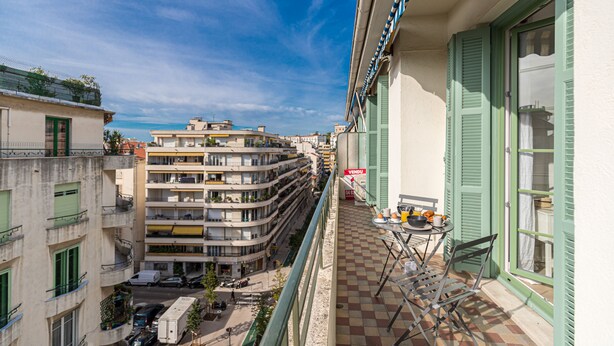 Ein Balkon mit Schachbrettboden, einem Tisch und Stühlen, und einem 'VENDU'-Schild.