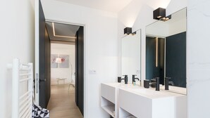 Ein modernes Badezimmer mit einem weißen Waschtisch, schwarzen Armaturen und einem großen Spiegel.