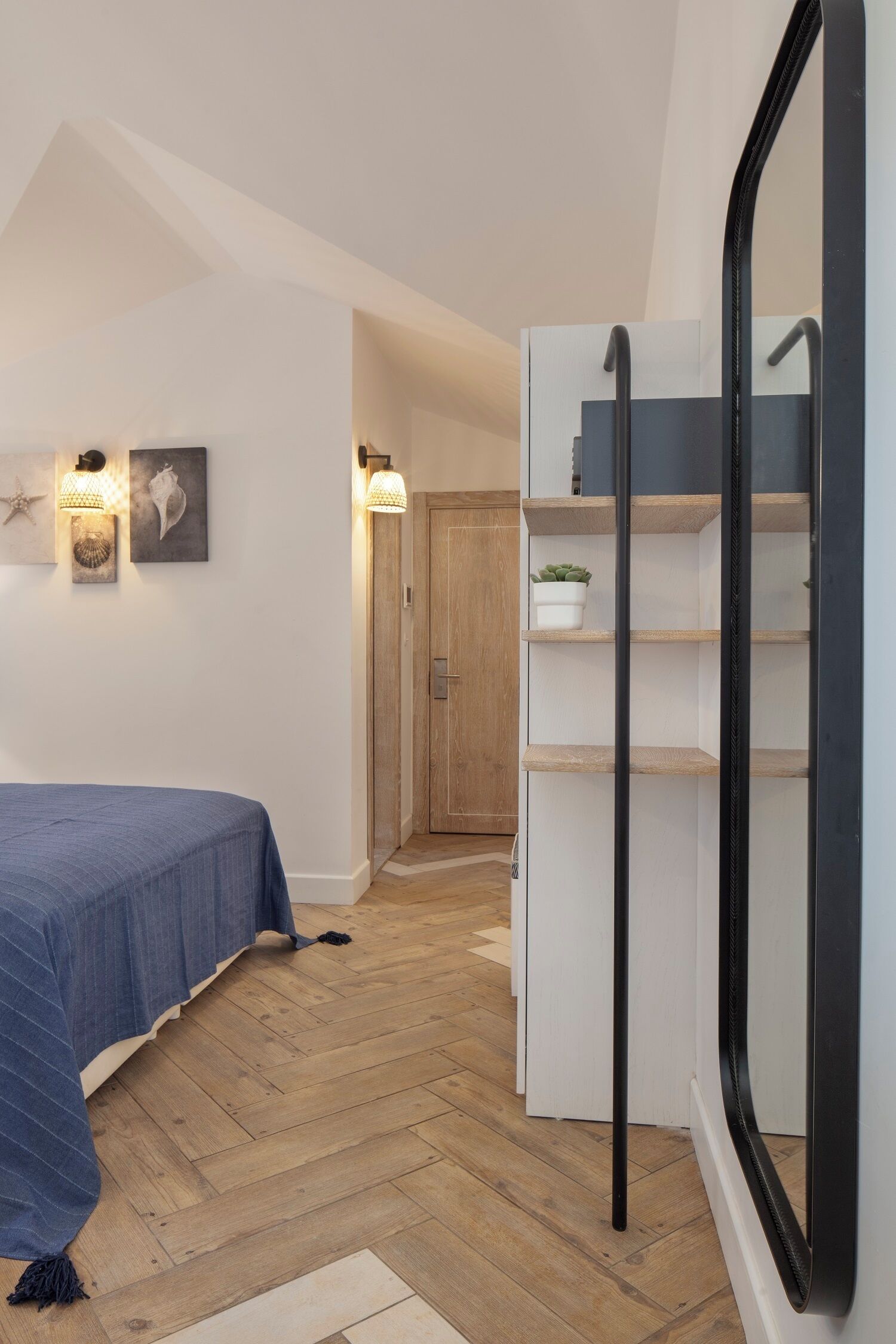 A bedroom with a bed, wooden flooring, a wardrobe, and a mirror.
