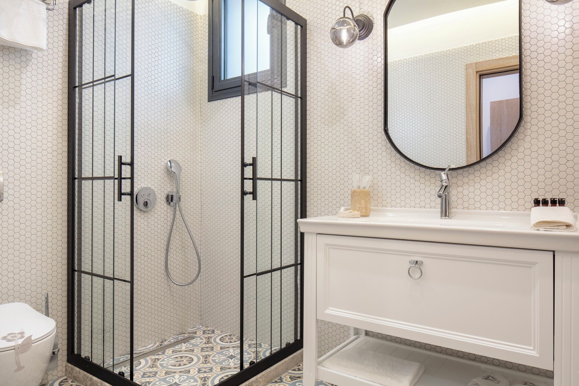 Un baño con cabina de ducha de vidrio, tocador blanco con espejo y un inodoro.