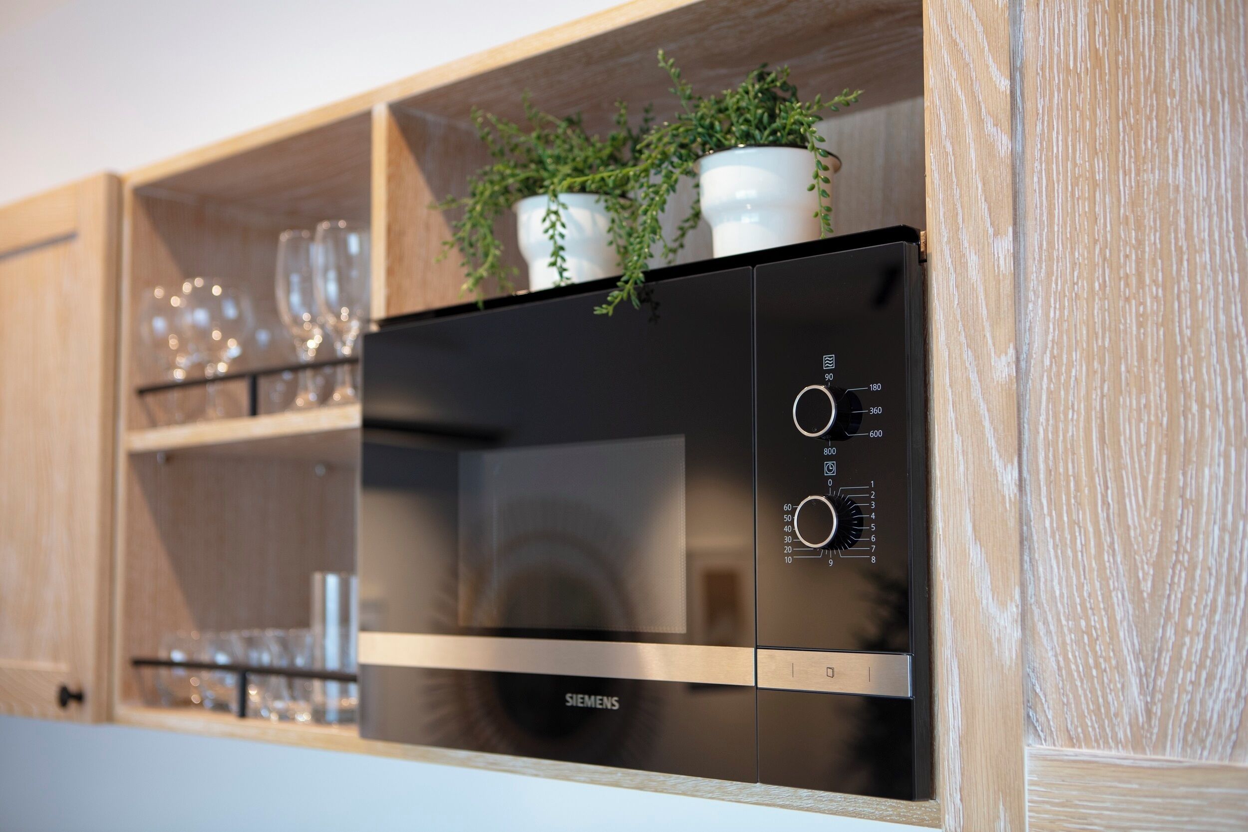 A kitchen with a black Siemens oven, wooden shelves, and potted plants.