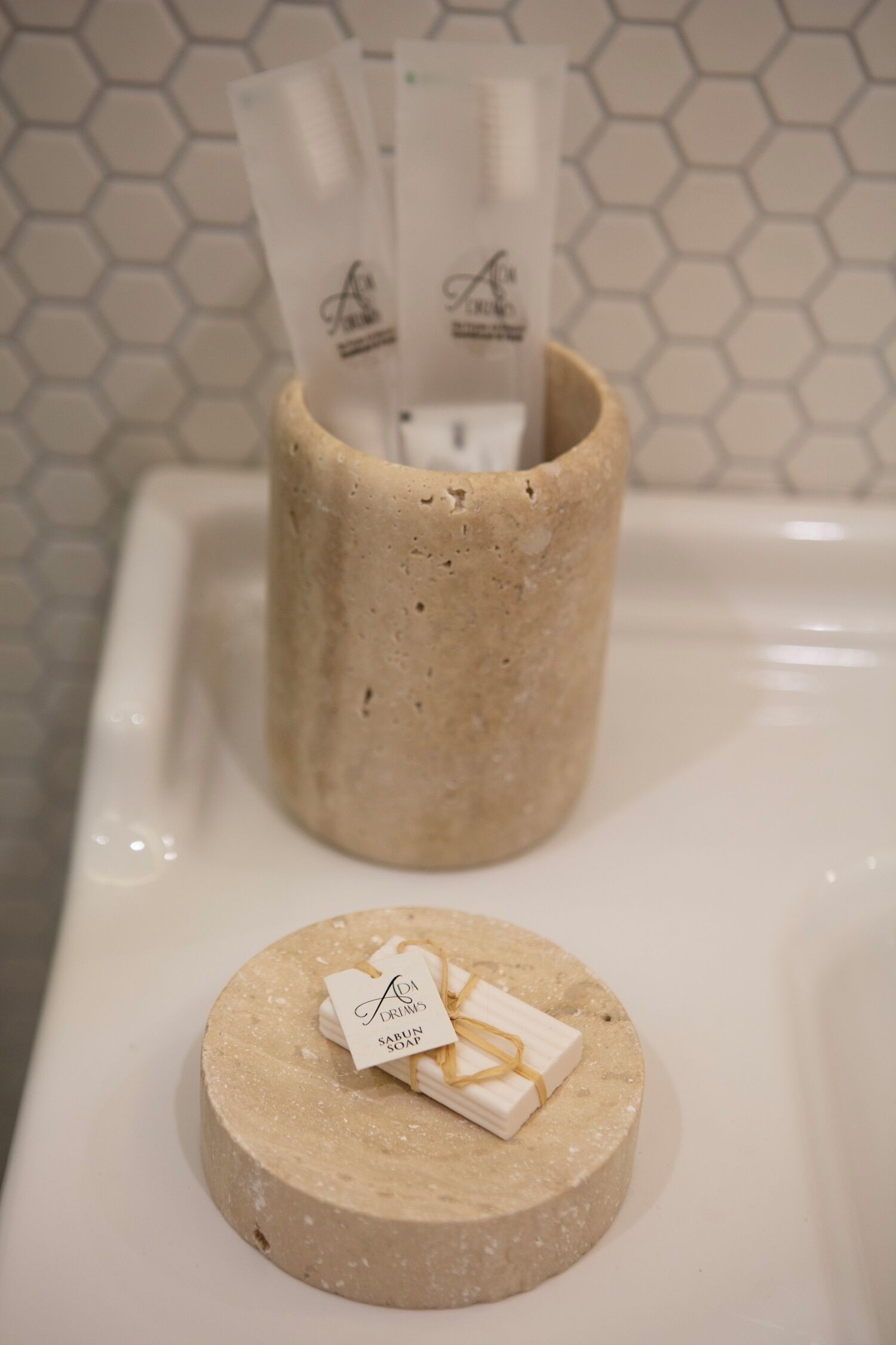 Une salle de bain avec un porte-savon beige contenant un pain de savon et un récipient rempli de dosettes de savon.