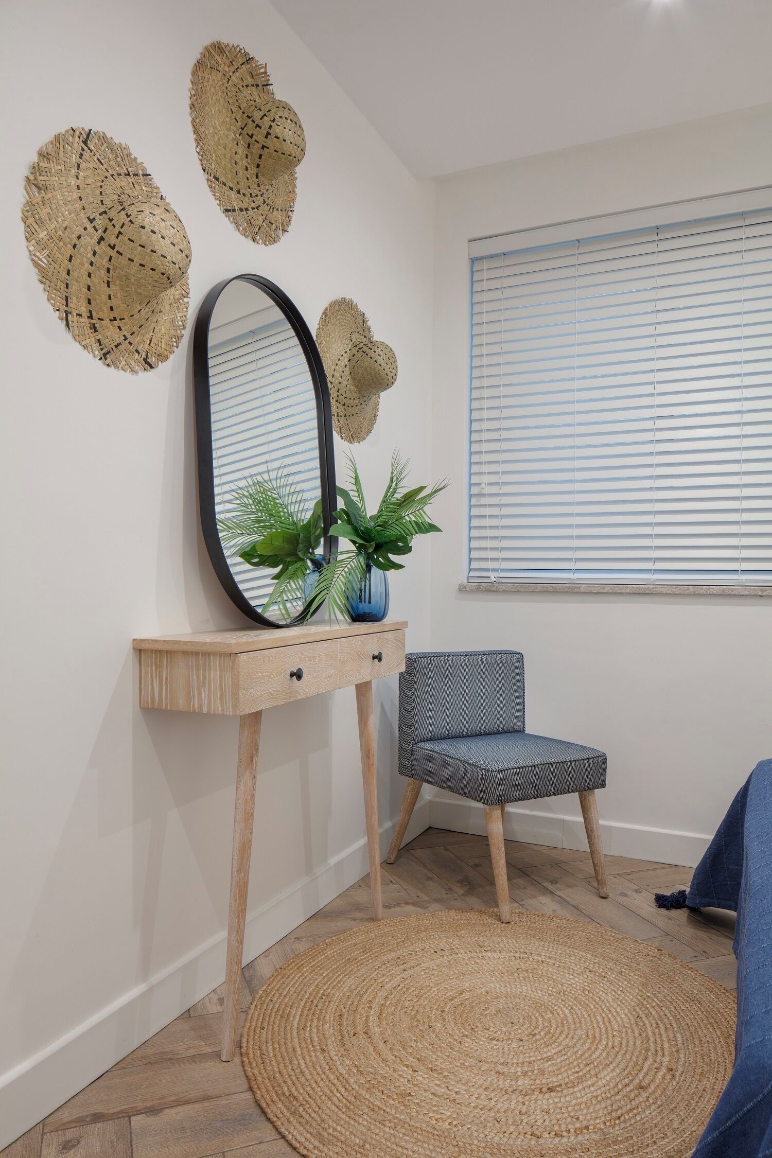 Una habitación con un tapete redondo tejido, una consola de madera con un espejo, una planta en maceta y una silla gris.