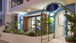 L’entrée d’un hôtel, avec une enseigne indiquant « Ada Dreams City », une porte d’entrée et un bac à fleurs contenant des plantes tropicales.