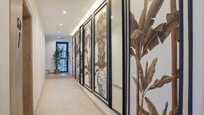 Un couloir orné de reproductions encadrées de motifs botaniques, une plante en pot et une porte en bois avec une pancarte.