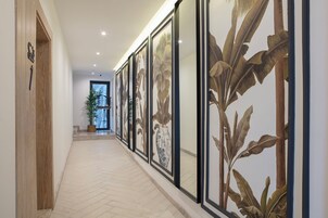 A hallway with framed botanical artwork on the walls, a potted plant, and a wooden door with a sign.