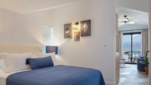 Une chambre à coucher comprenant un lit, une table de chevet, une lampe fixée au mur et une vue sur la mer depuis un balcon.
