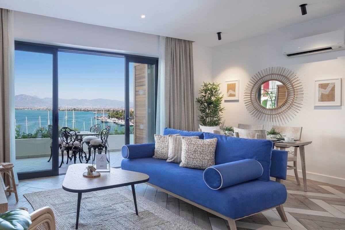 A modern living room with a blue sofa, a dining table, and a view of a marina.
