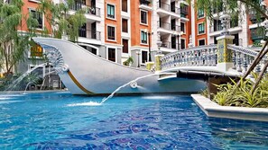 A swimming pool with a unique boat-shaped design, surrounded by multi-story buildings with balconies.