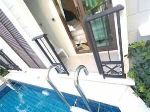 A poolside area with a glass balustrade, a white outdoor seating area, and a view of a building with a balcony.