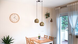 Un comedor con mesa y sillas de madera, un reloj de pared, lámparas colgantes y una planta en maceta.