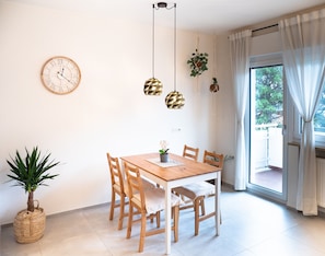 A dining area with a wooden table and chairs, a wall clock, hanging pendant lights, and a potted plant.