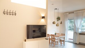 Una sala de estar moderna con televisor de pantalla plana, un comedor con sillas de madera y un amplio ventanal con cortinas.