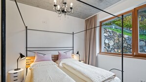 Una camera da letto con una struttura letto in metallo, due comodini, un lampadario, una finestra che si affaccia su un muro in pietra e un pavimento in legno.
