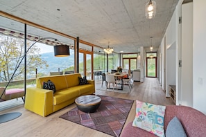 Un salon moderne avec un canapé jaune, une table basse ronde et une vue sur l’extérieur.