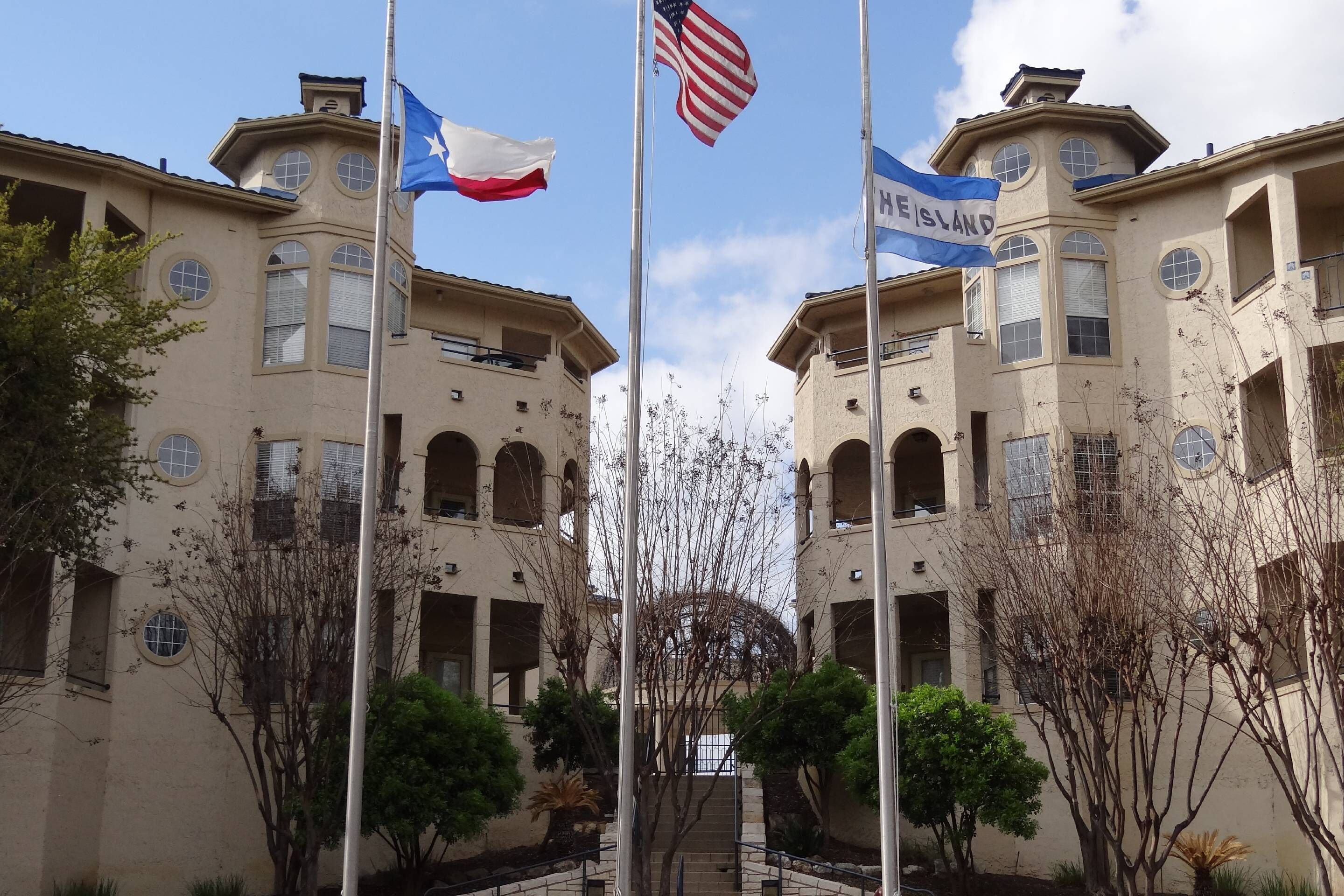 A building with multiple flags, including the American flag, a flag with a blue and white design, and a flag with the text "HISLAND".