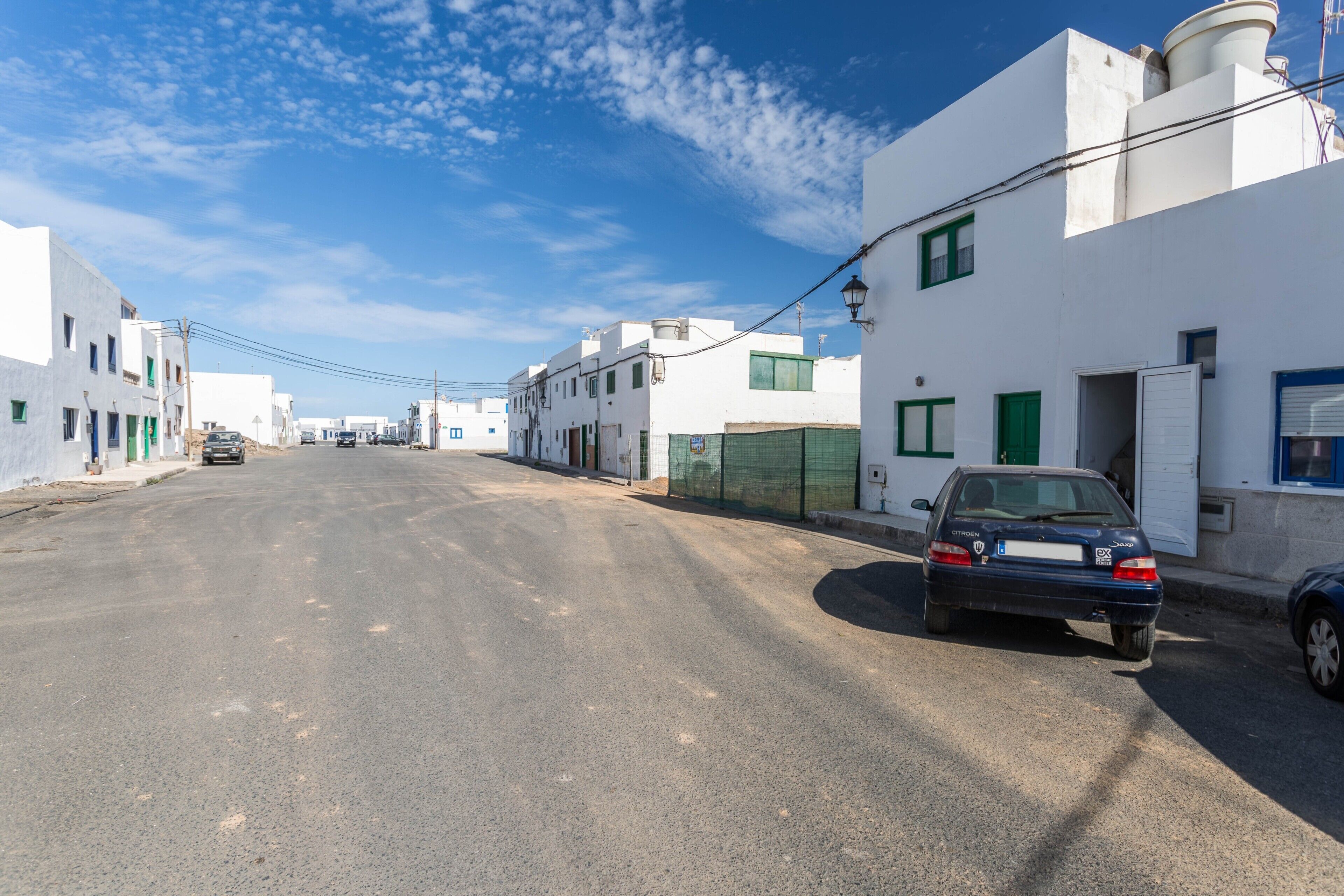 Una calle con edificios blancos, un coche aparcado y un cielo azul despejado.